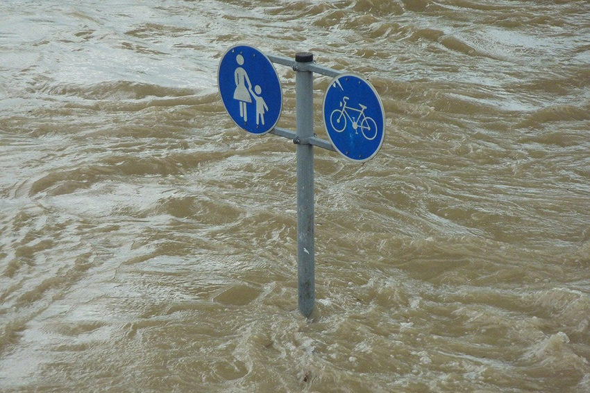 Aus den braunen Fluten ragen zwei Schilder für Fuß- und Radweg.