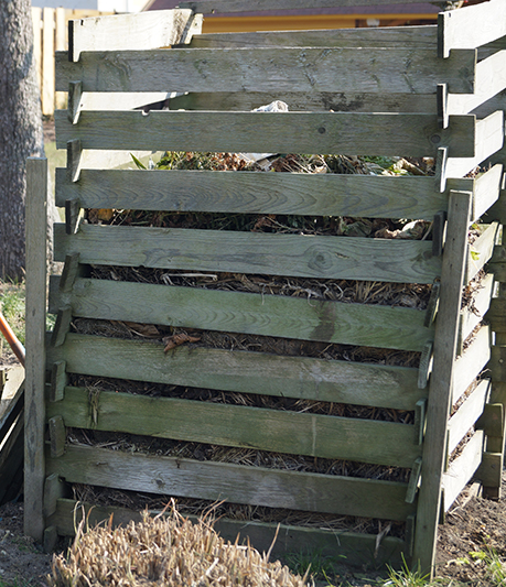 De hoge compostbak is gebouwd met houten planken en voor tweederde gevuld.