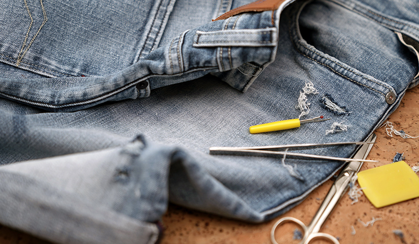 Eine Bio-Jeans liegt neben einer Schere und einem Reparaturset auf einem Tisch.