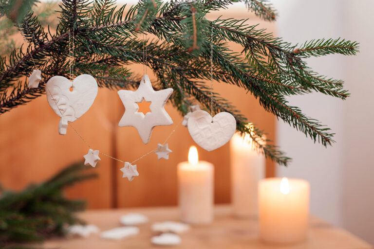 Baumschmuck aus Kaltporzellan hängt an einem Tannenzweig.