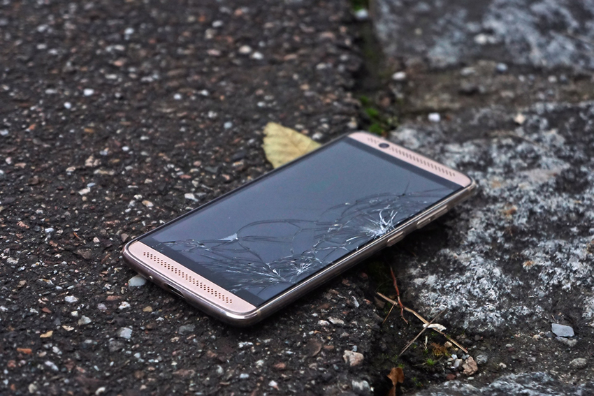 Ein Handy liegt mit zerbrochenem Display auf dem Asphalt.