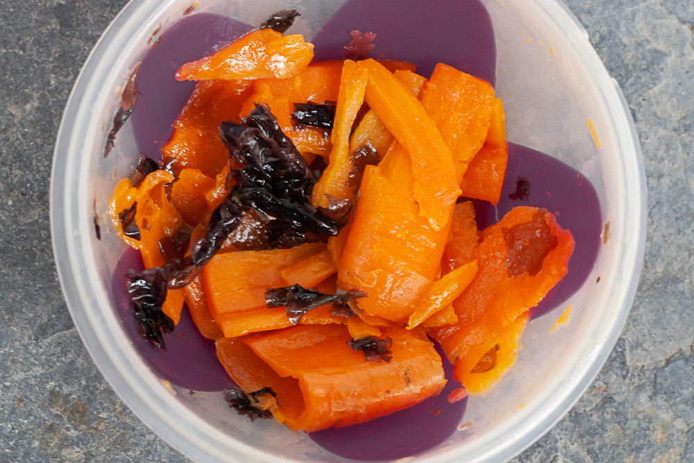 Die Karottenscheiben sind mit Öl benetzt und mit braunen Algen gemischt in einer offenen Dose zu sehen.