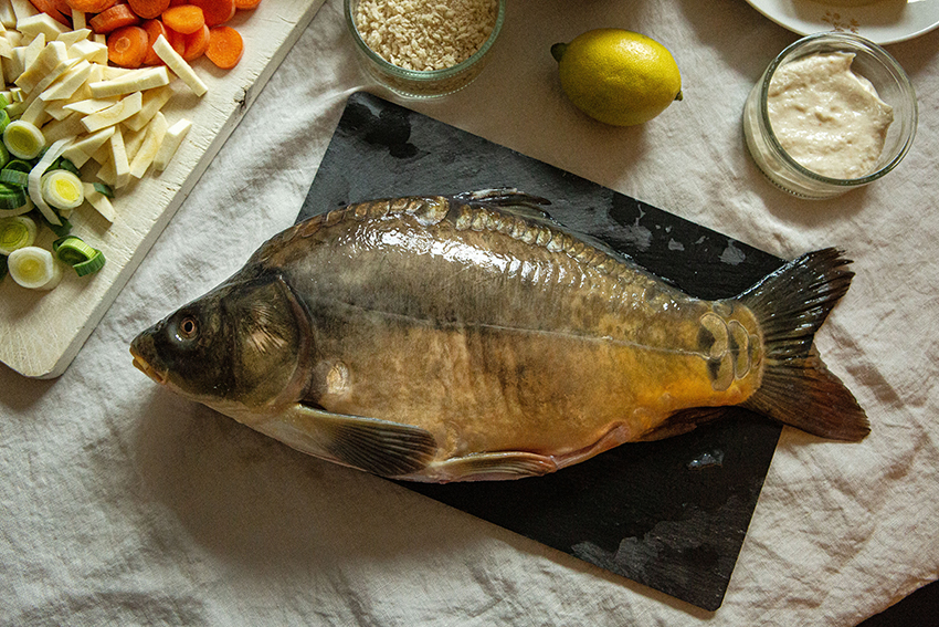 Der Karpfen liegt auf einer Schieferplatte, daneben sind weitere Zutaten für das Essen bereitgestellt.