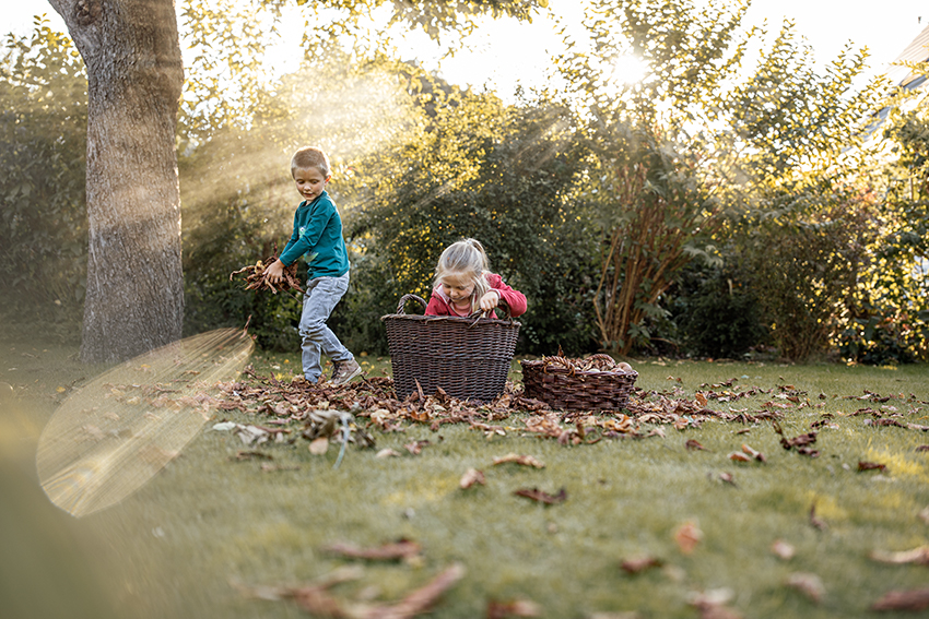 Zwei Kinder spielen im Garten mit einem Korb voll Laub.