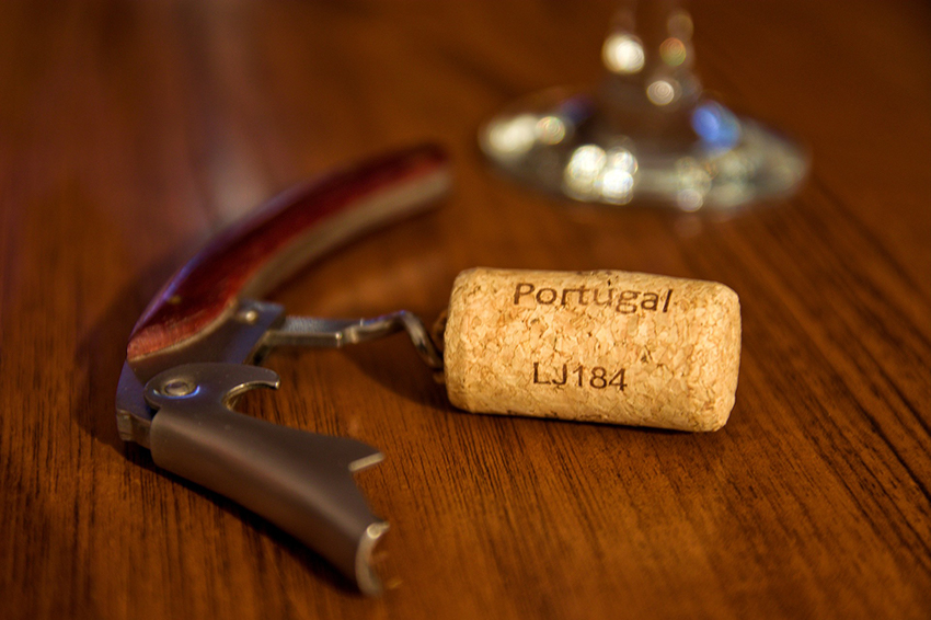 Een kurkentrekker ligt op een houten tafel, de eruit getrokken wijnkurk zit erop vast.
