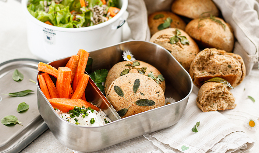 In einer Vesperbox aus Metall sind Brötchen, Karotten und Kräuterquark verstaut.