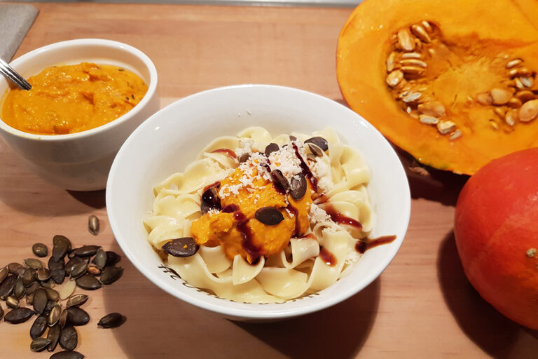 Die Bandnudeln in der Schale sind mit orangendem Pesto und Kürbiskernen getoppt.