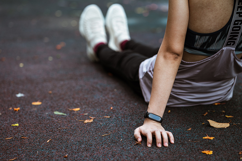 Eine Frau sitzt erschöpft vom Sport auf dem Asphalt und trägt einen Fitness-Tracker am Handgelenk.