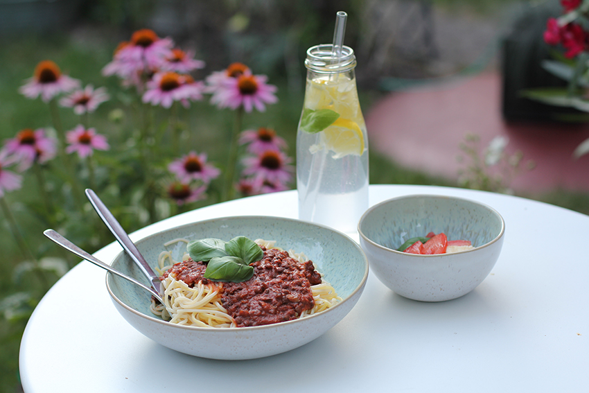 Ein Teller mit Spaghetti und veganer Linsenbolognese steht auf einem Gartentisch.