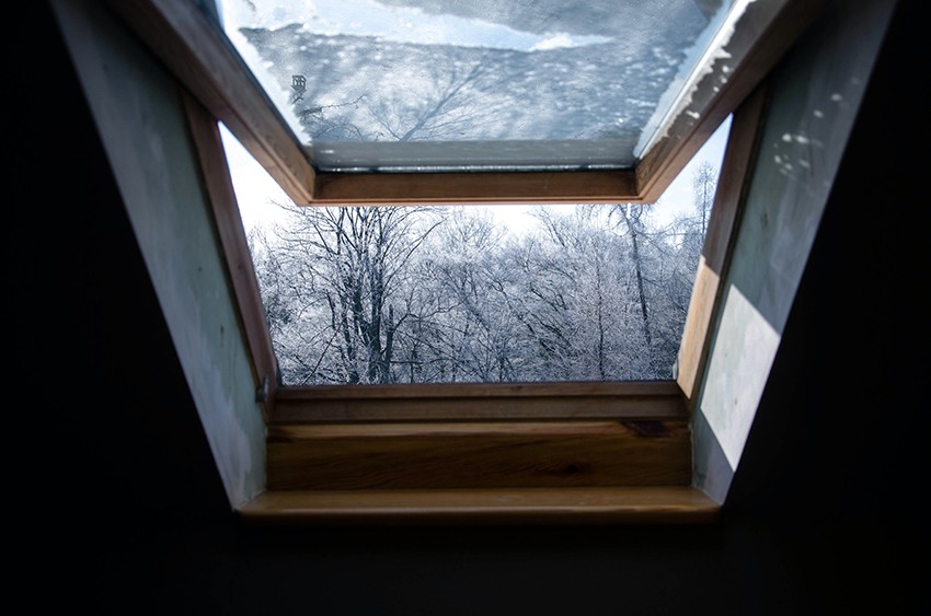 Ein Dachfenster ist geöffnet, draußen sieht man verschneite Bäume.