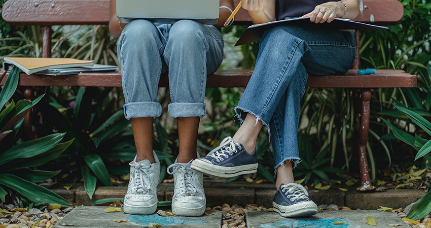 Twee meisjes zitten op een bankje in het park, beiden dragen een spijkerbroek.