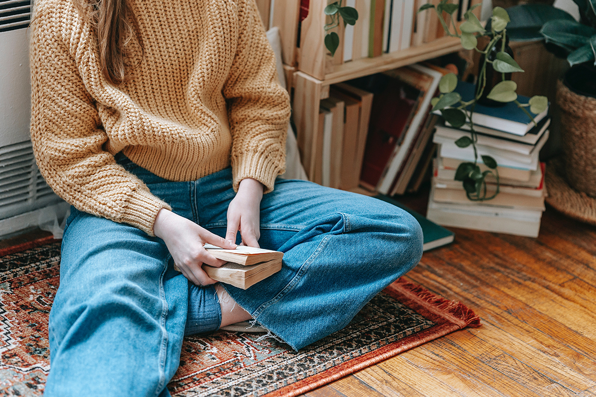 Ein Mädchen sitzt im Schneidersitz mit einem Buch in der Hand auf einem Teppich und trägt eine Bio-Jeans.