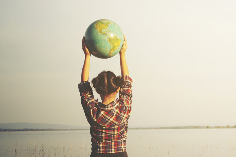 Ein Mädchen steht vor einem See und hält einen Globus in die Luft.