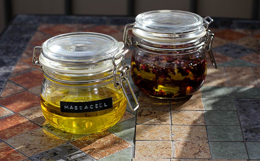 Zwei Glasdosen mit selbst gemachten Massageöl stehen auf einem bunten Gartentisch.