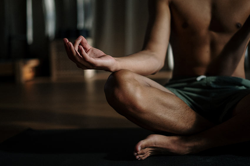 Ein Mann sitzt mit nacktem Oberkörper im Schneidersitz und meditiert.