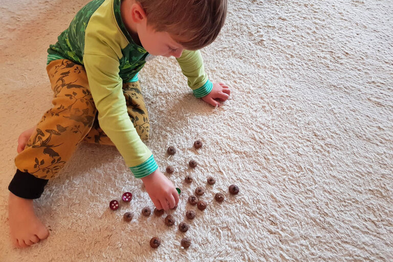 Der kleie Junge dreht ein Eichelhütchen um, auf der usche nach dem nächsten passenden Paar.