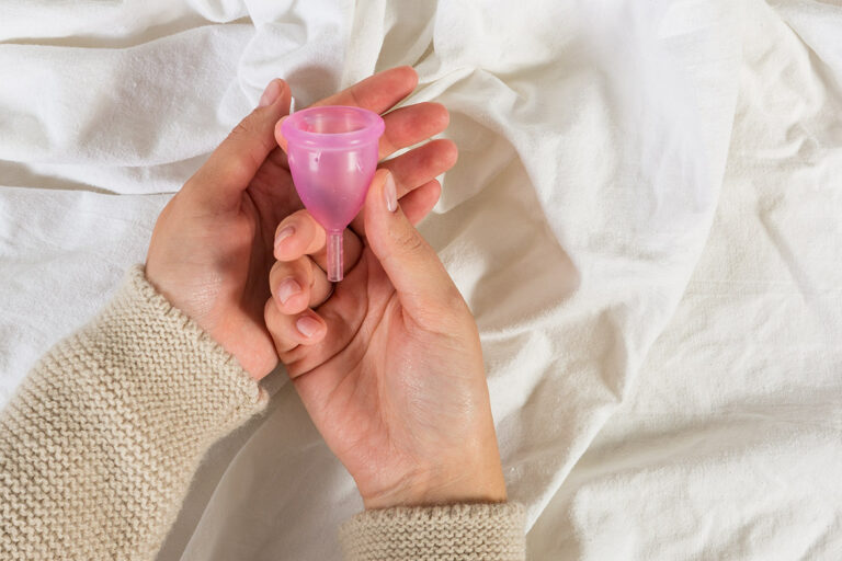 Zwei Hände halten eine rosafarbene Menstruationstasse
