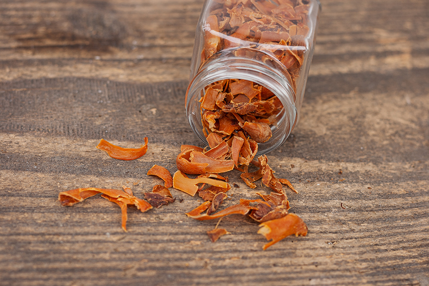 Die orangenen Stücke der Muskatblüte fallen aus einem kleinen Glas.