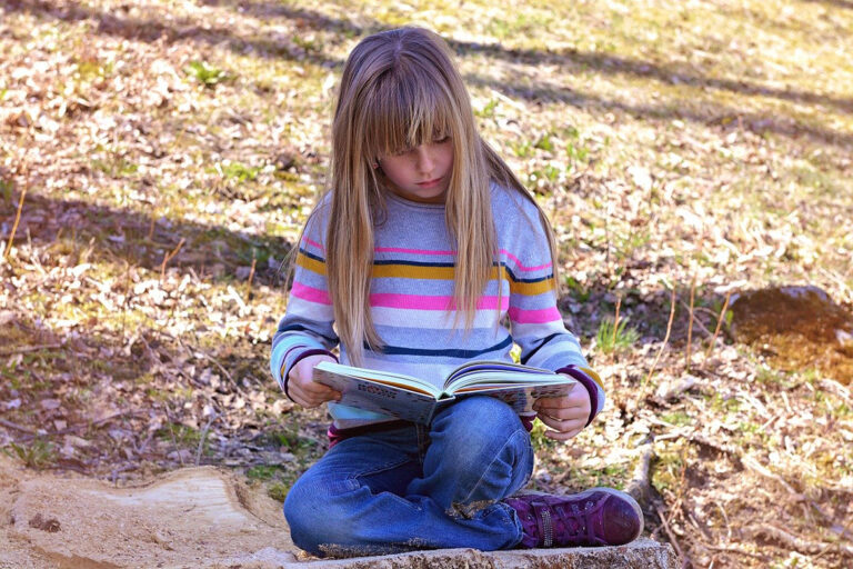 Ein Mädachen sitzt auf einem Holzstumpf und liest in einem Buch.