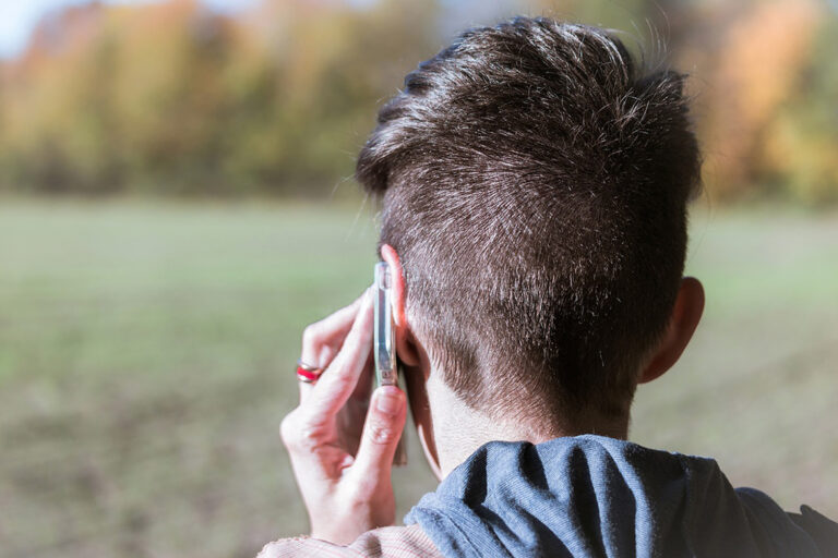 Das Foto zeigt einen Hinterkopf mit kurzen Haaren, an das linke Ohr wird ein Handy gehalten.