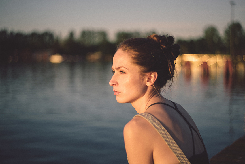 Frau schaut mit ernstem Gesicht auf einen See.