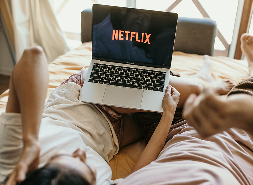 Ein Paar liegt im Bett und hat den Streaming-Dienst Netflix auf dem Laptop geöffnet, um den CO2-Fußabdruck des Internets zu senken.