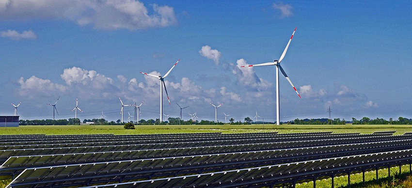 Hinter dem Solarfeld stehen Windräder.