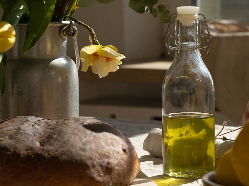 Eine Flasche mit Olivenöl steht neben einem Laib Brot auf dem Tisch.