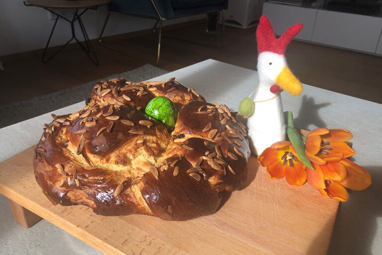 Das braun gebackene Osterbrot ist auf einem Holzbrett drapiert und von Osterdeko begleitet.