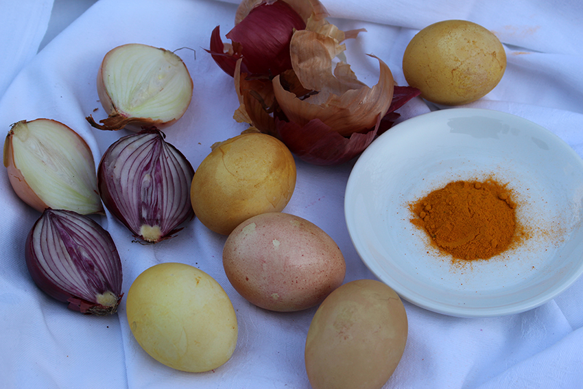 Eieren in verschillende tinten geel liggen naast kurkumapoeder, uien en uienschillen.