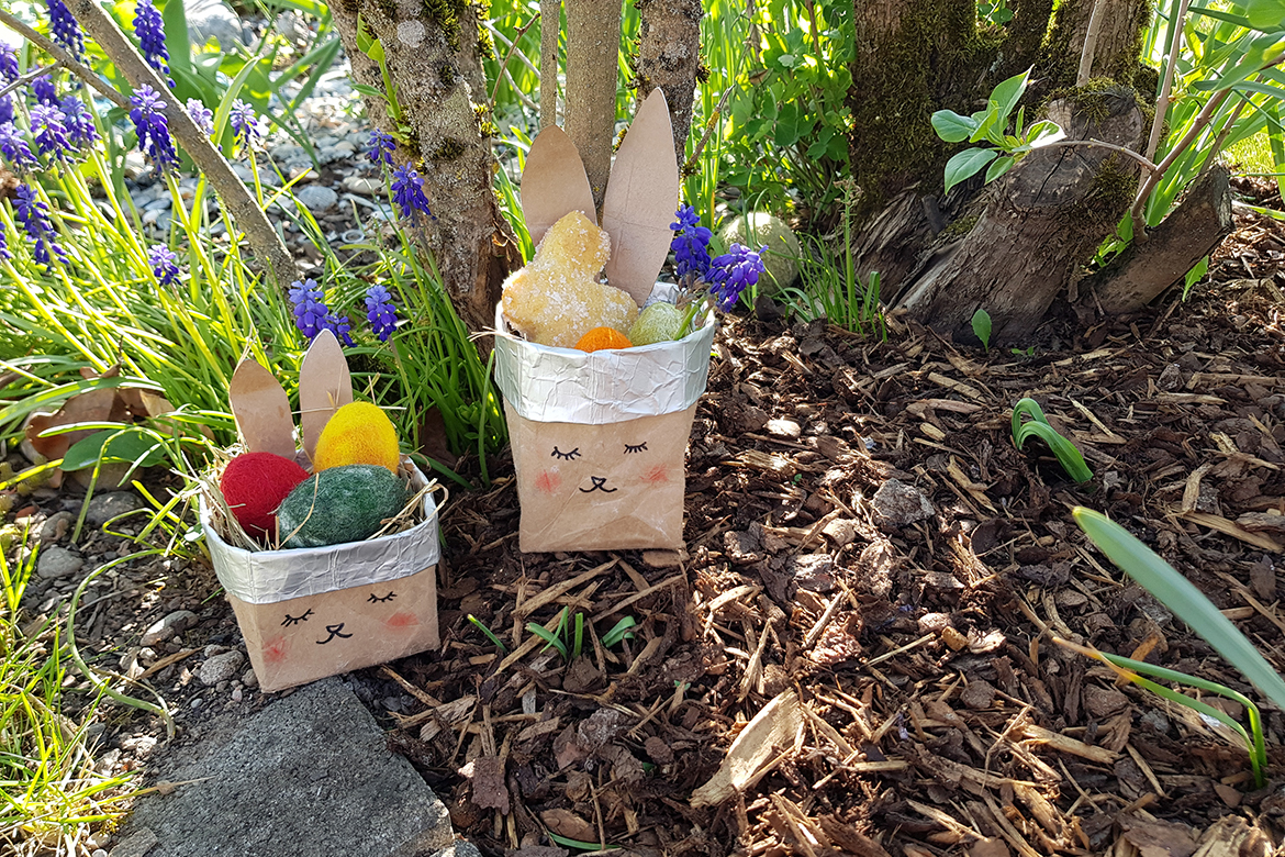 Ein kleines und ein größeres Osternest aus einem Milchkarton stehen im Garten.