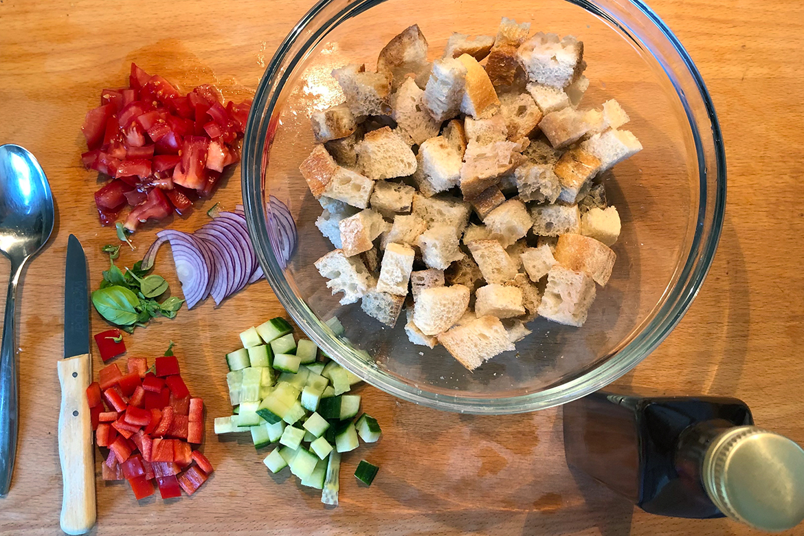 Die Zutaten für die Panzanella liegen auf dem Küchenthresen aus Holz, das Brot ist bereits in einer Schüssel.