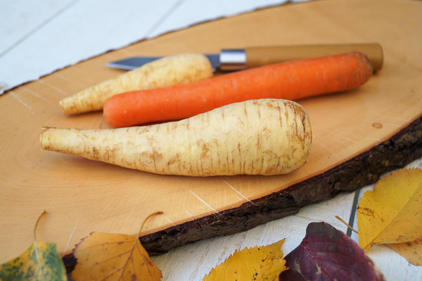 Zwei Pastinaken und eine Karotte liegen auf einem Schneidebrett aus Holz.