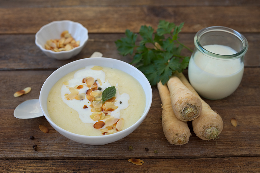 Selbst gemachte Petersilienwurzel-Suppe samt Zutaten steht auf einem Holztisch.