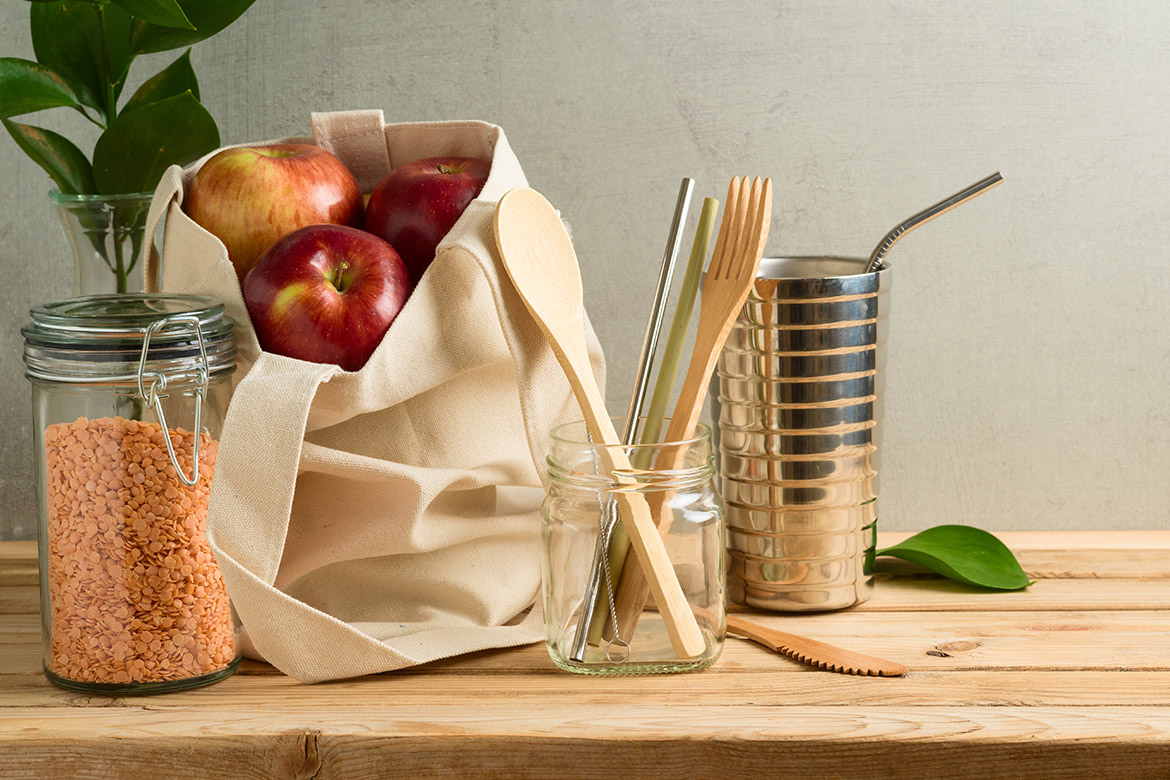 Rote Linsen im Glas, rote Äpfel im Beutel, Holz-Besteck und Edelstahl-Becher mit Edelstahl-Trinkhalm auf einem Holztisch