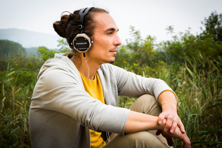 Ein Mann sitzt in der Natur und hört Podcast mit Kopfhörern.