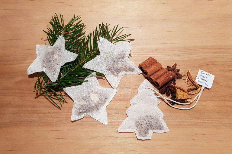 Drei Punschgewürz-Sterne und ein selbst genähter Teebeute-Tannenbaum liegen auf dem dekorierten Holzbrett.