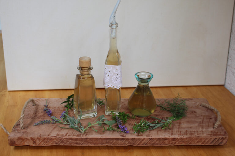 Drei Glasflaschen mit dem Raumduft aus Kräutern stehen auf einem Holzbrettchen.
