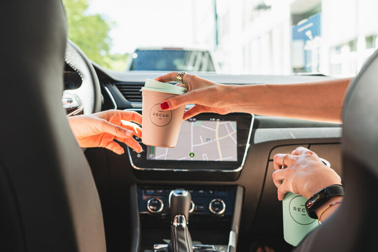 RECUP Kaffeebecher wird in einem Auto dem Fahrenden gereicht.