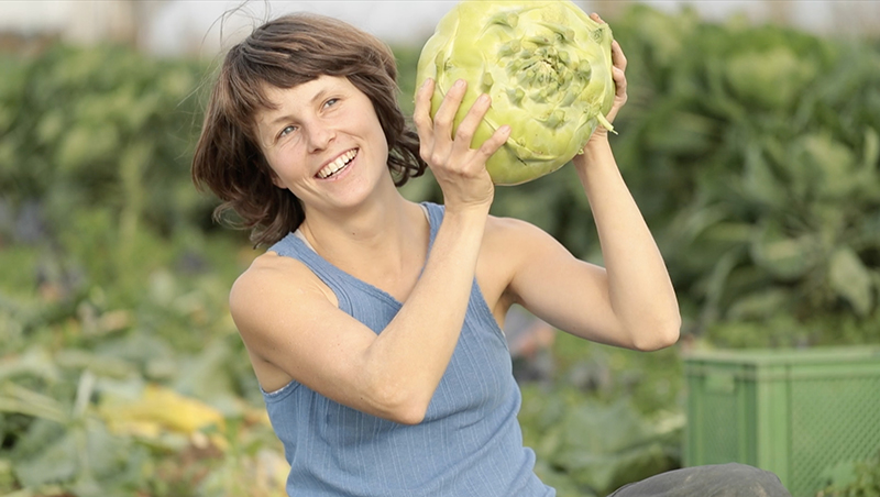 Eine Frau hält einen riesigen kohlrabi auf dem Feld hoch.