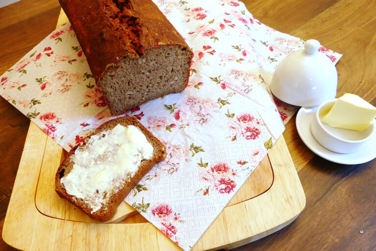 Das aufgeschnittne Brot wird flankiert von einer mit Butter bestrichenen Scheibe und einem Butterdöschen.
