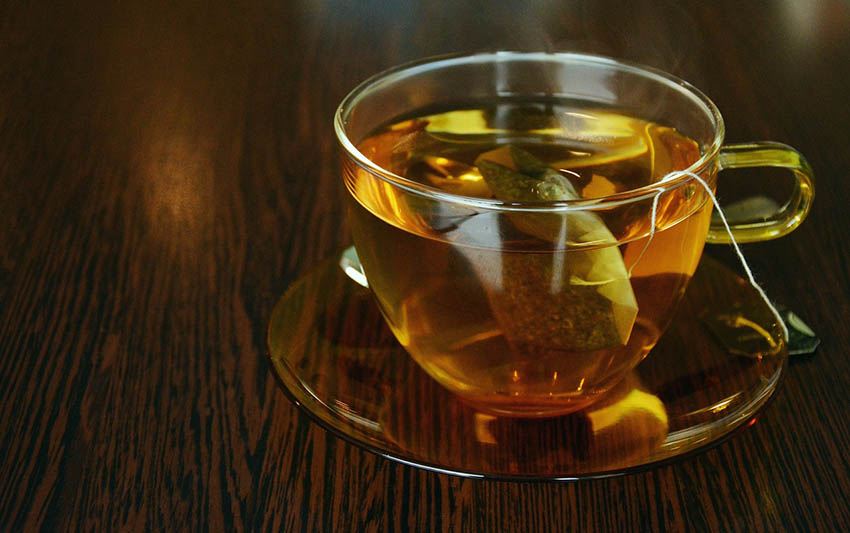 Tasse mit Teebeutel und Tee auf dunklem Holz