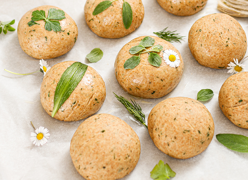 Selbst gebackene Brötchen mit Wildkräutern liegen auf einem Leinentuch.