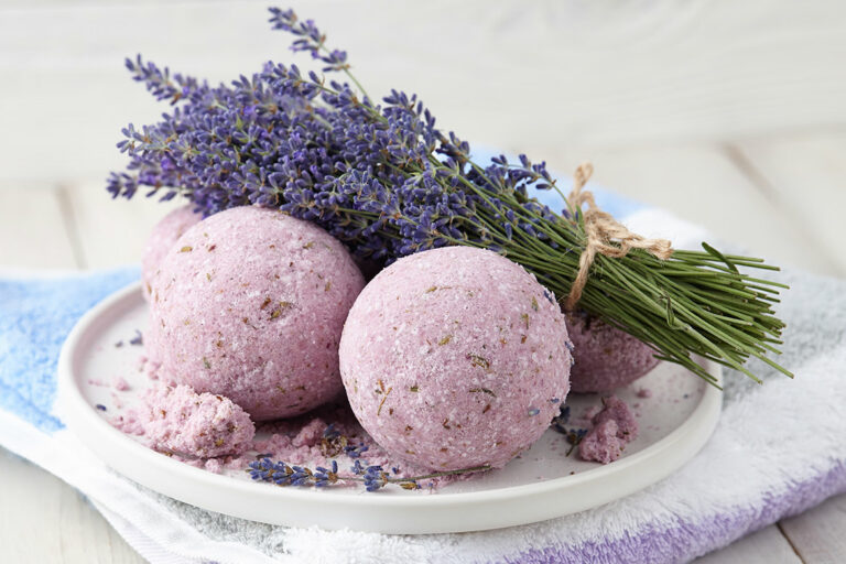 Violette Badekugeln mit einem Lavendel-Sträußchen auf einem weißen Teller