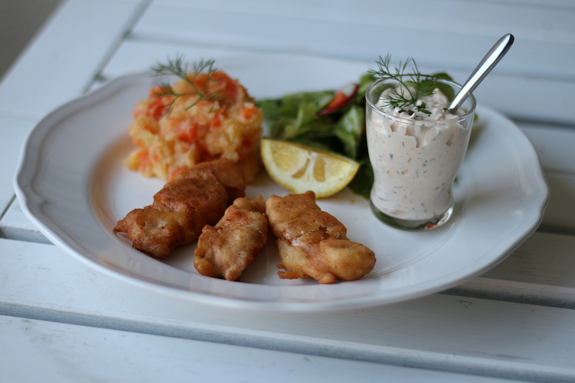 Selbst gemachte Fischstäbchen mit Kartoffelsalat und Remoulade sind auf einem Teller angerichtet.