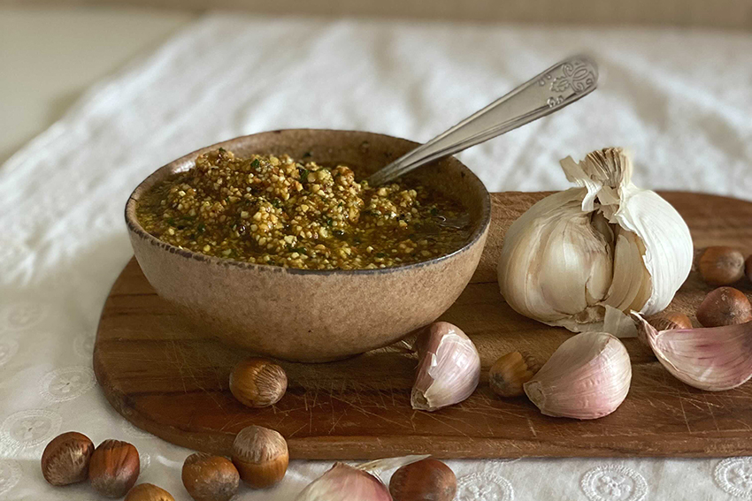 Eine Schüssel mit dem selbst gemachten Haselnusspesto steht bereit, Haselnüsse und Knoblauch liegen daneben.