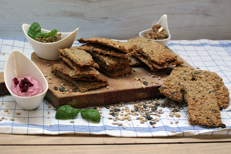 Selbst gemachtes Knäckebrot liegt auf einem Holzbrett, neben dem Dips in kleinen Schalen stehen.