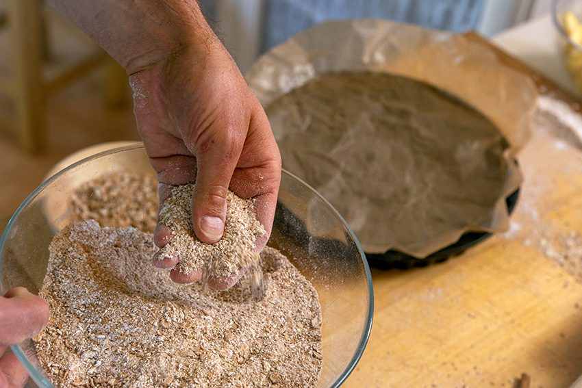 Selbst gemahlenes Mehl in einer Glasschüssel, eine Hand zerreibt das Mehl zwischen den Fingern.