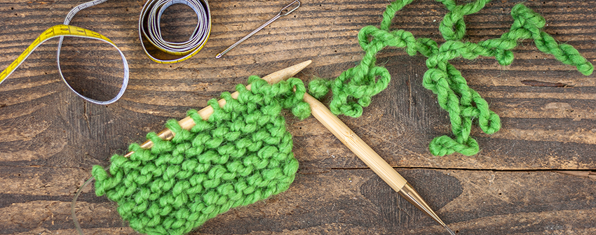 Die ersten gestrickten Reihen grüner Wolle liegen auf der Nadel.