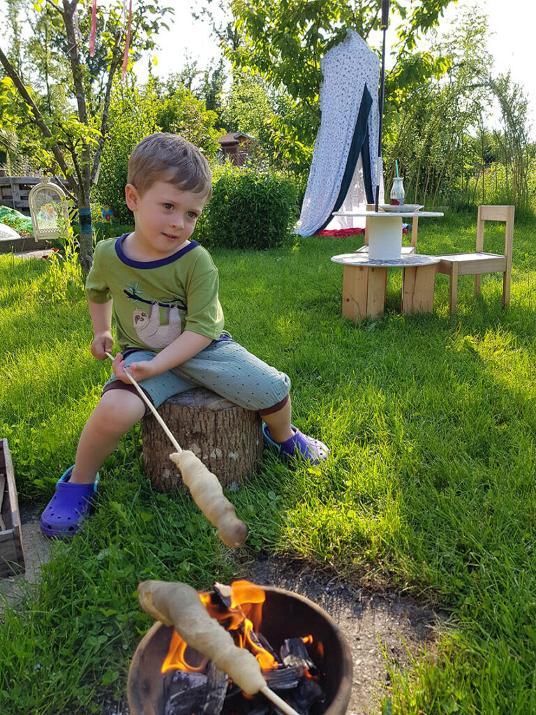 Der kleine Junge hält das Stockbrot über das Feuer.